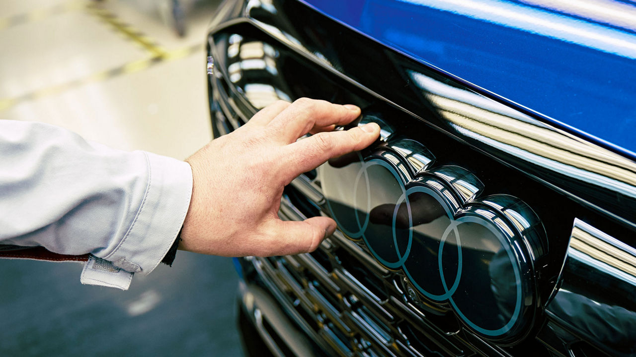 Eine Hand berührt das Audi Logo an einer Fahrzeugfront